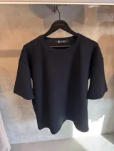 Remera negra de algodón con textura, cuello redondo y mangas cortas.