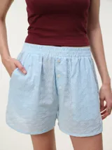 Short celeste confeccionado en broderie de algodón, con diseño liviano, cintura elastizada y detalles de botones frontales.