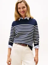 Sweater de punto fino en algodón, con diseño de rayas horizontales en azul marino y blanco. Presenta cuello redondo, mangas largas con puños acanalados y detalle de botones dorados en uno de los hombros.