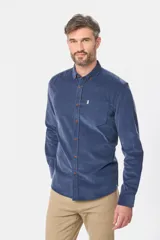 Camisa de pana fina en color verde oscuro, de manga larga con puños arremangados, cuello camisero con botones y un bolsillo aplicado en el pecho con pequeña etiqueta decorativa.