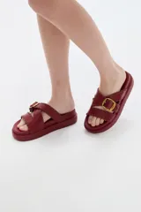 Sandalias planas de eco cuero color bordó, con tiras cruzadas y hebilla metálica dorada.