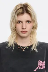 Collar de doble cadena, una de perlas irregulares y otra de eslabones dorados con pequeñas bolitas. La cadena dorada tiene dijes colgantes en forma de corazón esmaltados en varios colores (marrón, vino, verde menta, rosa pálido). El cierre es tipo toggle dorado.