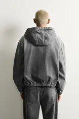 Cazadora de denim con efecto lavado, corte relajado, cierre frontal de cremallera, capucha, bolsillos tipo canguro y acabados elásticos en puños y bajo.