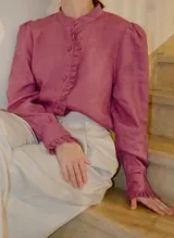 Blusa de lino color rosado, con cuello alto mao, mangas largas abullonadas con volados en los puños y detalles de volados frontales junto a la botonadura.