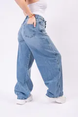Pantalón de jean wide leg en lavado azul claro vintage, con corte amplio y fluido. Presenta un cierre asimétrico con botones expuestos en la parte delantera, talle alto y bolsillos funcionales.