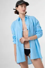 Camisa de algodón color beige, de corte holgado y diseño oversize, con cuello camisero, mangas largas, bolsillo frontal y cierre de botones de madera.