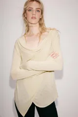 Chaqueta de punto fino color beige, con escote fluido y drapeado, manga larga y cierre frontal cruzado.