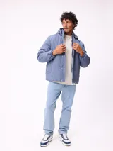 Campera puffer Rusty de color azul, con capucha desmontable, cierre frontal con botones a presión y bolsillos laterales. Presenta un parche con el logo de la marca en el pecho.