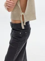 Chaleco marrón de punto con cuello alto y detalle de flecos en el pecho.