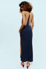 Vestido midi de tejido elástico color azul marino, con cuello halter, aberturas en la espalda y detalle de aplique metálico.