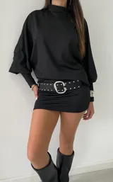 Vestido corto negro de cuello alto, con mangas largas abullonadas y puños ajustados. El diseño presenta un corte entallado en la falda y un estilo minimalista.
