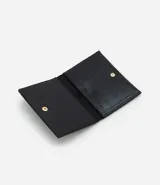 Billetera pequeña tipo sobre de la marca Satinato, confeccionada en poliuretano texturizado color negro. Presenta un diseño compacto con cierre de botón metálico dorado y un interior organizado con divisiones para tarjetas.