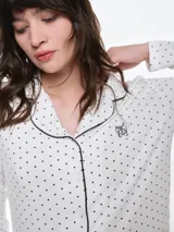 Camisa de pijama de manga larga con cuello solapa y cierre frontal de botones. Presenta un estampado sutil de pequeños corazones sobre una base de color gris melange, con detalles de ribete en contraste en el cuello y la botonera.
