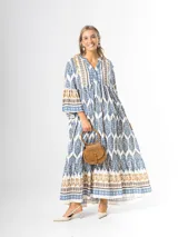 Maxi vestido largo de fibrana en color blanco con estampado paisley y geométrico en tonos azules y tostados, con escote en V, mangas largas amplias y diseño holgado con volados en la falda.
