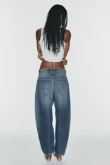 Jeans de tiro medio y corte barrel con diseño de perneras curvadas, tiro medio, trabillas para cinturón y cinco bolsillos. Presenta lavado clásico y costuras pespunteadas decorativas en la parte delantera.