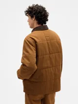 Campera acolchada de color marrón, con cierre frontal de botones a presión, cuello de pana en tono más oscuro y bolsillos frontales tipo parche.