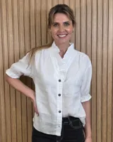 Camisa de lino color blanco, con cuello con volados, botones oscuros en contraste y mangas cortas abullonadas con puños elastizados.