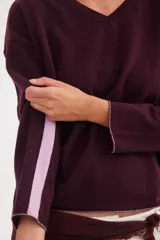 Buzo de escote en V confeccionado en lana, con mangas largas y diseño básico. Presenta una raya vertical en contratono en una de las mangas y detalles de color en los puños y el ruedo.