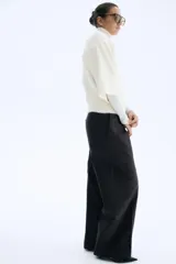 Saco de punto suave color crema, con cuello camisero y cierre frontal de botones marrones. Presenta hombros caídos y mangas holgadas por debajo del codo.