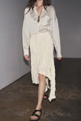 Falda midi color crudo, de tiro medio y confeccionada en viscosa. Presenta detalle de pliegues y bajo asimétrico. Cierre lateral con cremallera oculta.