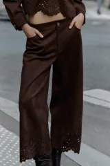 Pantalón culotte marrón de tiro alto con efecto ante, bolsillos delanteros y traseros, pernera ancha y corta. El bajo está troquelado con un diseño floral. Cierre frontal con cremallera y botón.