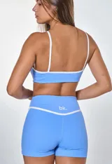 Conjunto deportivo compuesto por un top y un short de color celeste con detalles en blanco. El top tiene breteles finos y el logo 'bk.' estampado en el frente. El short es de tiro alto con una banda blanca horizontal en la cintura y líneas laterales blancas.