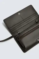 Cartera tipo bandolera de piel color marrón oscuro, con solapa y cierre a presión. Incluye seis ranuras para tarjetas, una ranura para billetes y un monedero interior con cierre de cremallera. Posee un asa de hombro ajustable y extraíble.