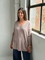 Sweater de punto color visón con escote en V, mangas largas con puños acanalados, corte holgado y dos bolsillos frontales tipo parche.