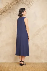 Vestido midi azul con textura crepé, escote en V, sin mangas, bolsillos laterales y aplique de flor con piedras facetadas en el escote.