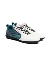 Championes de fútbol Umbro modelo Vision TF, diseñados para césped sintético. Presentan una combinación de colores blanco, verde azulado y detalles en fucsia, con el logo de la marca en el lateral y suela de goma con tapones pequeños.