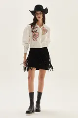 Camisa blanca de algodón con bordados florales en tonos rosados y rojizos en el frente. Presenta mangas largas abullonadas y puños con bordado.