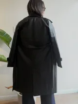 Trench de ecocuero negro con diseño cruzado de doble abotonadura, solapas clásicas, puños ajustables y largo midi.