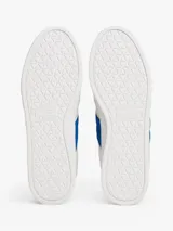 Zapatillas deportivas de estilo vintage Tommy Jeans modelo The Greenwich, confeccionadas en ante color blanco con paneles laterales en azul vibrante y detalles en gamuza gris claro. Presentan cierre con cordones, suela cupsole de goma y logo de la marca en el lateral.