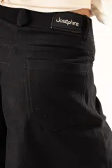 Pantalón de corte palazzo en color negro, con cintura alta, cierre frontal con botón y costuras verticales que definen su estructura amplia.