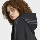 Campera corta Adidas SST 2.0 de color negro, con capucha, cierre frontal de cremallera bidireccional y las clásicas tres tiras en las mangas.