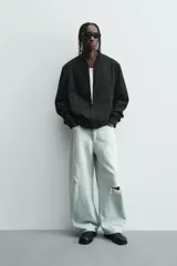 Cazadora bomber negra de corte regular fit, confeccionada en tejido efecto ante. Cuenta con cuello, puños y bajo en rib elástico, manga larga, bolsillos de vivo en la cadera y un bolsillo interior. Cierre frontal con cremallera.