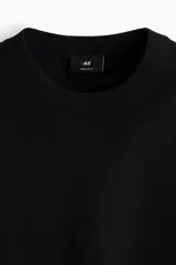 Buzo negro de punto fino con cuello redondo, mangas largas y remates acanalados en cuello, puños y bajo. Corte estándar.