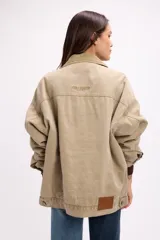 Campera de denim color marrón con diseño vintage, corte relajado y cuello de pana al tono. Presenta cierre frontal con botones metálicos, bolsillos con solapa en el pecho y bolsillos laterales.