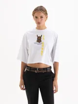 Remera blanca de corte cropped y manga corta, confeccionada en algodón. Presenta una estampa frontal con un conejo con estampado animal print sobre una nube y el texto 'IL BUNNY' en color amarillo.