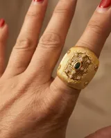 Anillo ancho de bronce con baño de oro, diseño texturizado con detalles calados tipo filigrana, incrustaciones de circonitas y una piedra verde central ovalada.