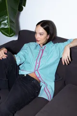 Camisa verde con rayas verticales blancas y detalles de zigzag rosa en el frente.