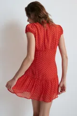 Vestido corto rojo con estampado de lunares blancos, cuello redondo con escote en pico pronunciado, manga muy corta y cierre frontal con botones.