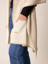 Poncho abierto de tejido de punto en color gris claro con bordes y detalles de bolsillos en gris oscuro. Presenta un diseño holgado y versátil con placa metálica decorativa en uno de los bolsillos frontales.