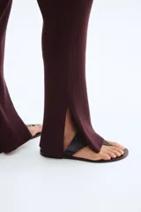 Pantalón de tiro alto, color marrón oscuro, confeccionado en tejido de punto acanalado. Presenta elástico oculto en la cintura y bajos acampanados con abertura lateral.