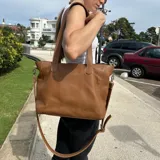 Cartera tipo tote de cuero natural color camel, con textura granulada. Cuenta con doble asa fija para llevar al hombro, correa larga ajustable y removible, cierre superior y bolsillo externo con cierre en la parte trasera.