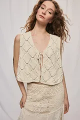 Chaleco corto de algodón color beige, confeccionado con un diseño calado en rombos, escote en V y cierre frontal con lazo para anudar.