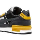 Championes urbanos Puma modelo Graviton Pro, con diseño inspirado en el running. Presentan una combinación de paneles en gris oscuro y gris claro, con detalles vibrantes en color naranja en los ojales, el talón y la pieza estabilizadora de la entresuela. Cuentan con suela blanca y cordones claros.