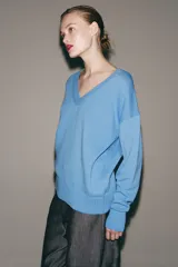 Sweater de punto color celeste, con escote en V y mangas largas con hombros caídos. Presenta terminaciones en rib en cuello, puños y ruedo.