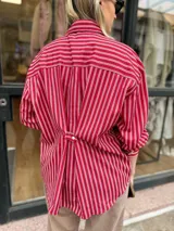Camisa oversize con diseño de rayas verticales rojas y blancas, de manga larga con puños abotonados y cierre frontal con botones.