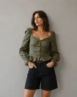 Top de mangas largas abullonadas con escote corazón y cierre frontal de botones. Presenta un diseño ajustado en el torso con un pequeño volado en el ruedo y estampado animal print en tonos verde oliva y negro.